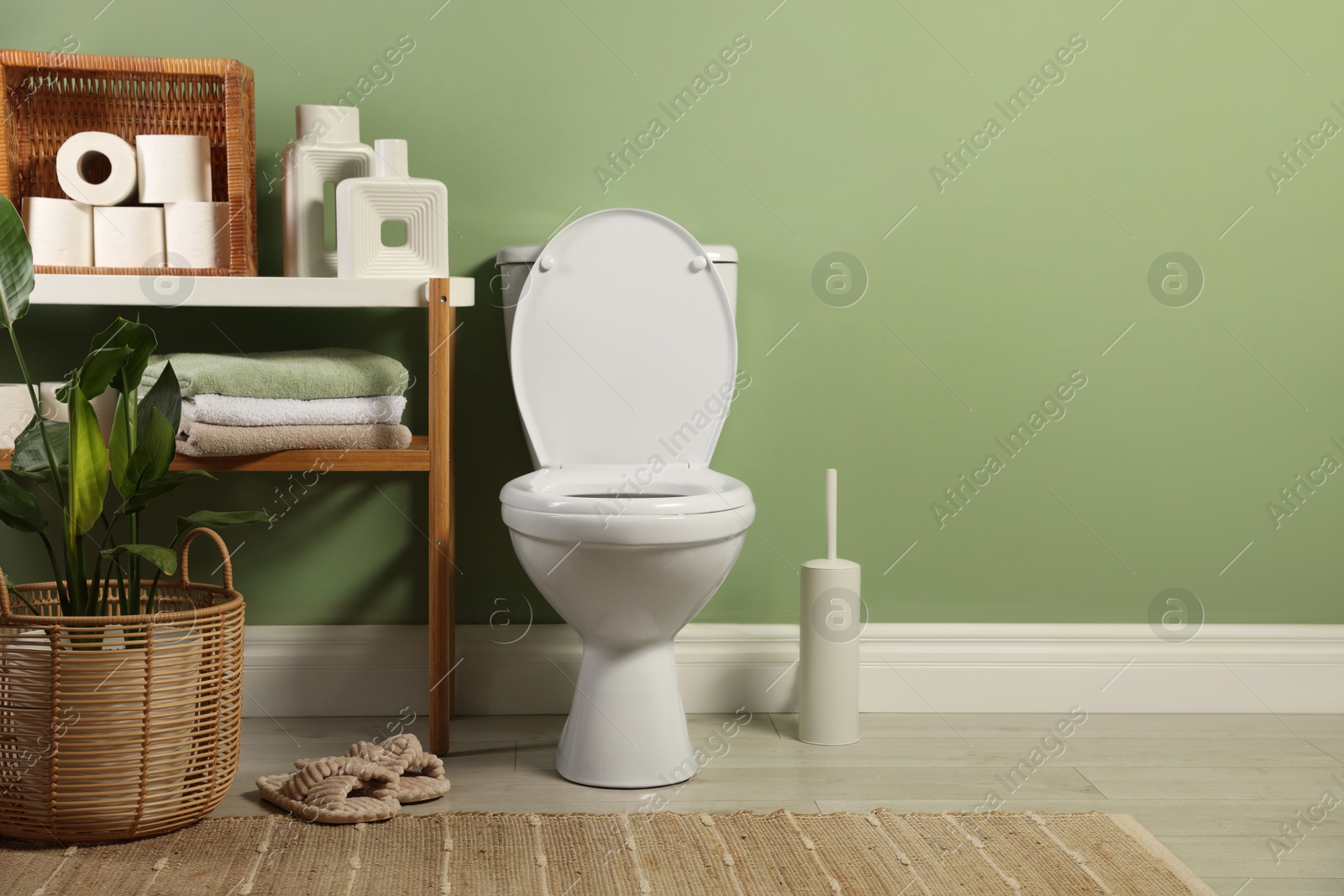 Photo of White toilet bowl, paper rolls, slippers and houseplants in bathroom, space for text