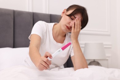 Worried young woman with pregnancy test on bed at home, selective focus