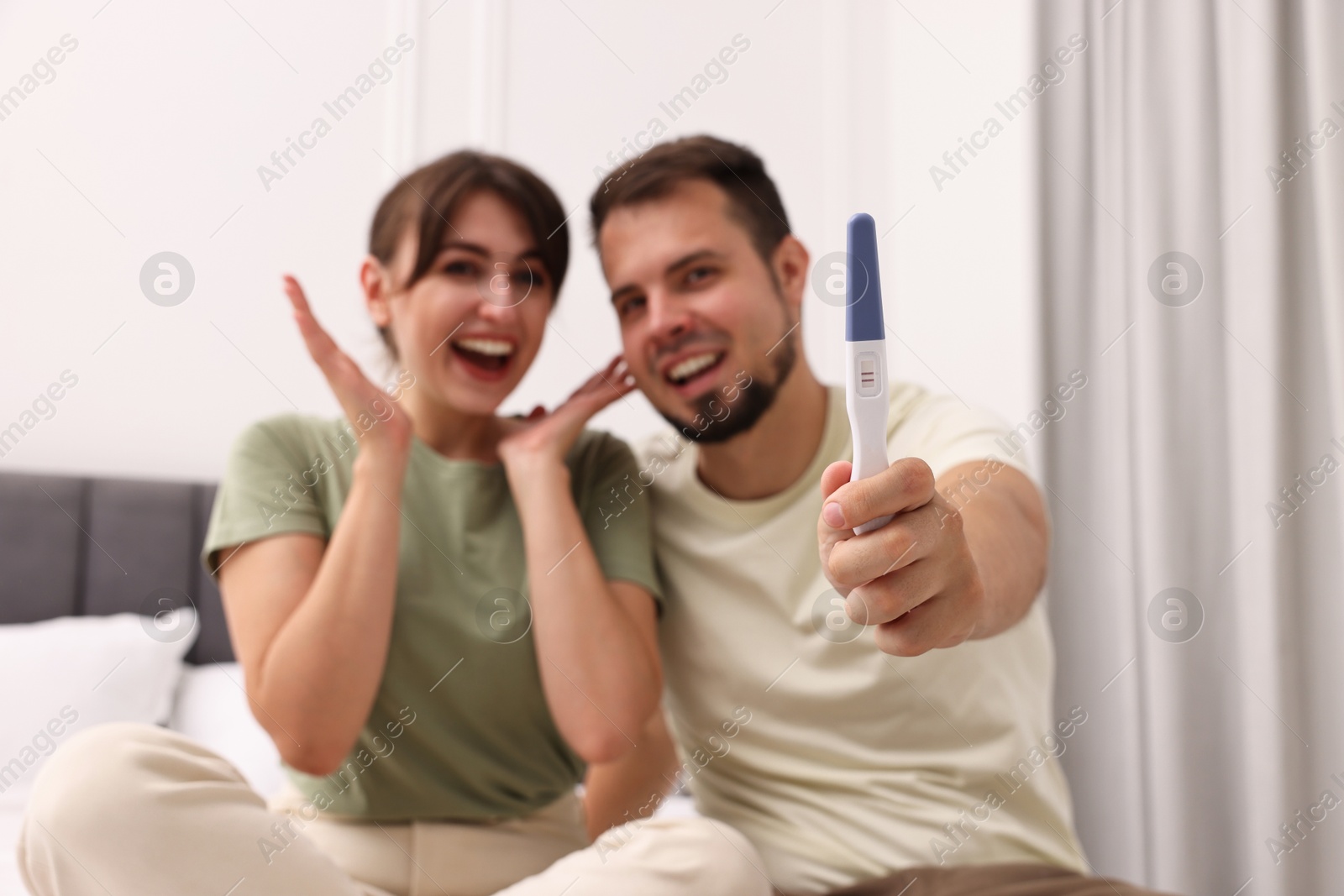 Photo of Happy young couple with pregnancy test at home, selective focus