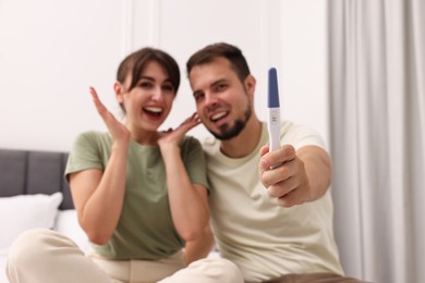 Photo of Happy young couple with pregnancy test at home, selective focus