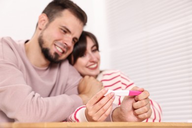 Happy young couple with pregnancy test at wooden table indoors, selective focus