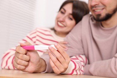 Happy young couple with pregnancy test at wooden table indoors, selective focus