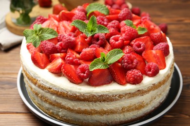 Photo of Tasty sponge cake with fresh berries and mint on wooden table, closeup