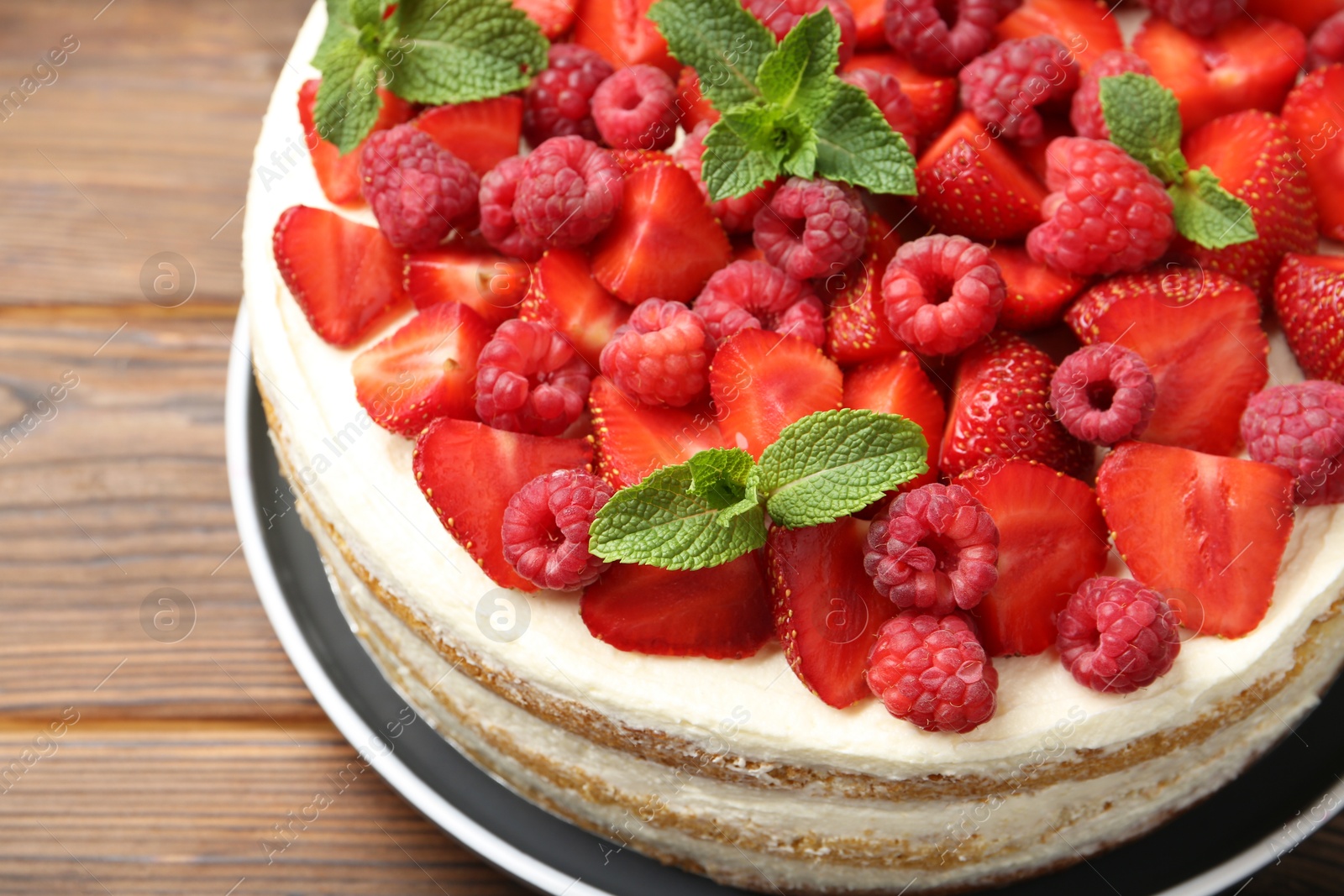 Photo of Tasty sponge cake with fresh berries and mint on wooden table, closeup