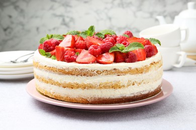 Photo of Tasty sponge cake with fresh berries and mint on light gray table