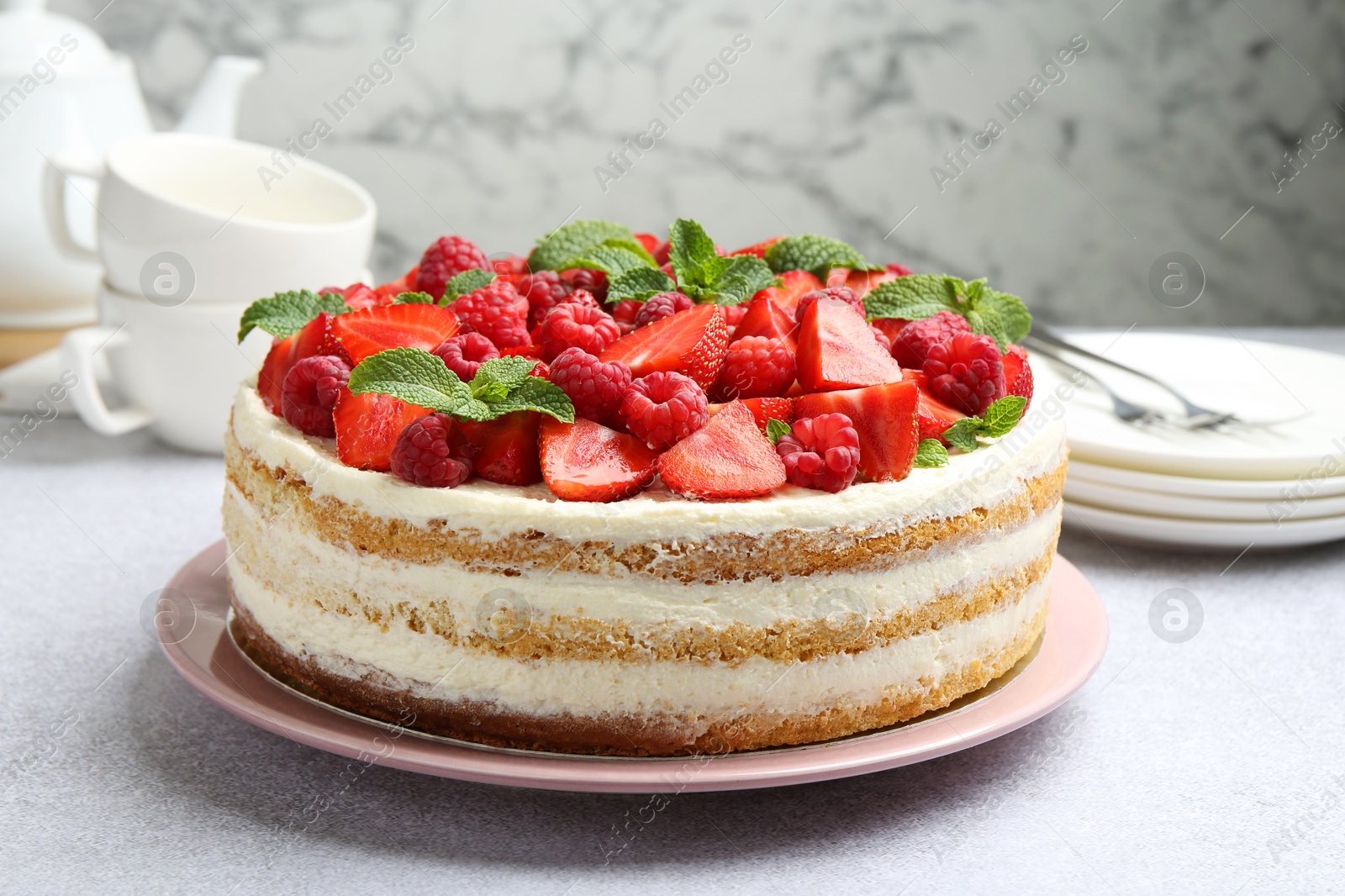 Photo of Tasty sponge cake with fresh berries and mint on light gray table