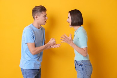 Emotional young couple arguing on orange background