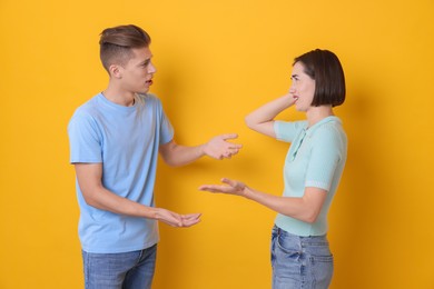 Emotional young couple arguing on orange background