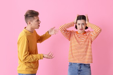 Emotional young couple arguing on pink background