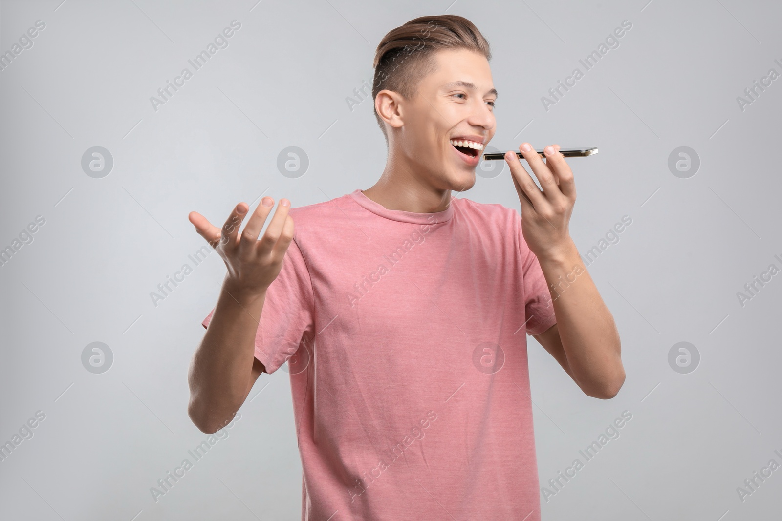 Photo of Young man recording voice message via smartphone on light gray background