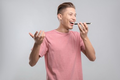 Young man recording voice message via smartphone on light gray background