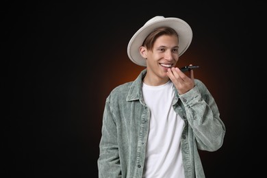 Photo of Young man recording voice message via smartphone on dark background, space for text