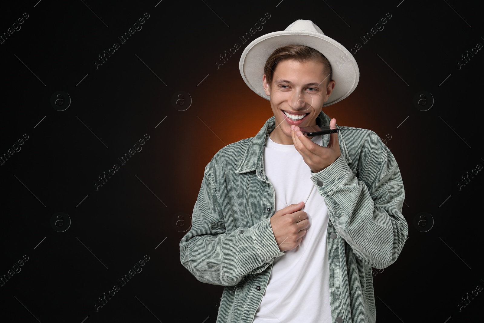 Photo of Young man recording voice message via smartphone on dark background, space for text