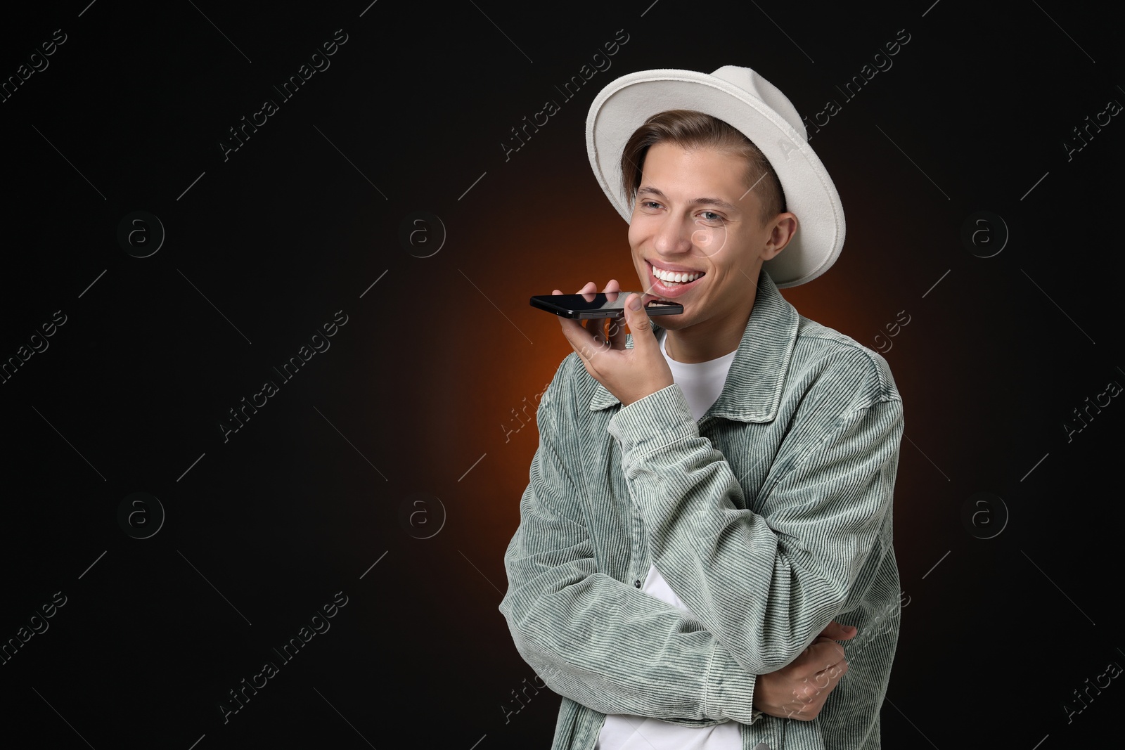 Photo of Young man recording voice message via smartphone on dark background, space for text