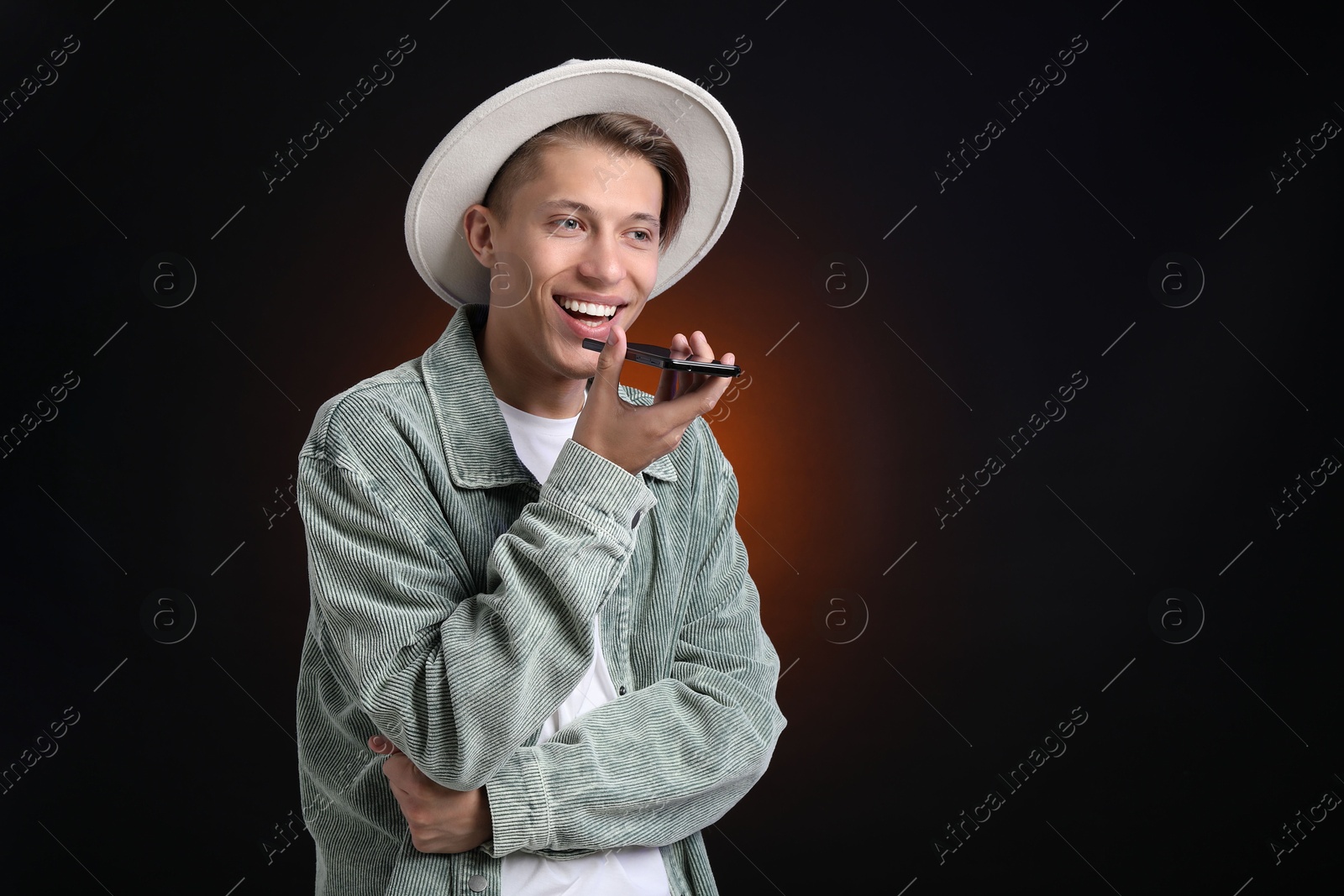 Photo of Young man recording voice message via smartphone on dark background, space for text