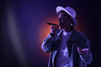 Photo of Young man recording voice message via smartphone on color background with neon lights, space for text