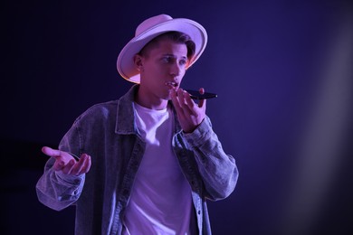 Photo of Young man recording voice message via smartphone on color background with neon lights, space for text