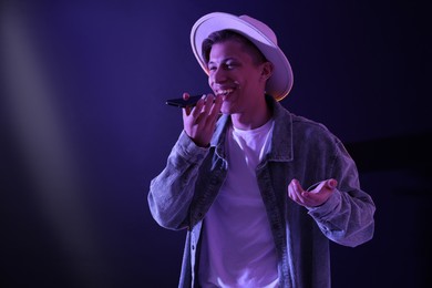 Young man recording voice message via smartphone on color background with neon lights, space for text