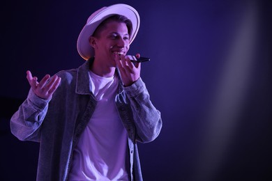 Photo of Young man recording voice message via smartphone on color background with neon lights, space for text