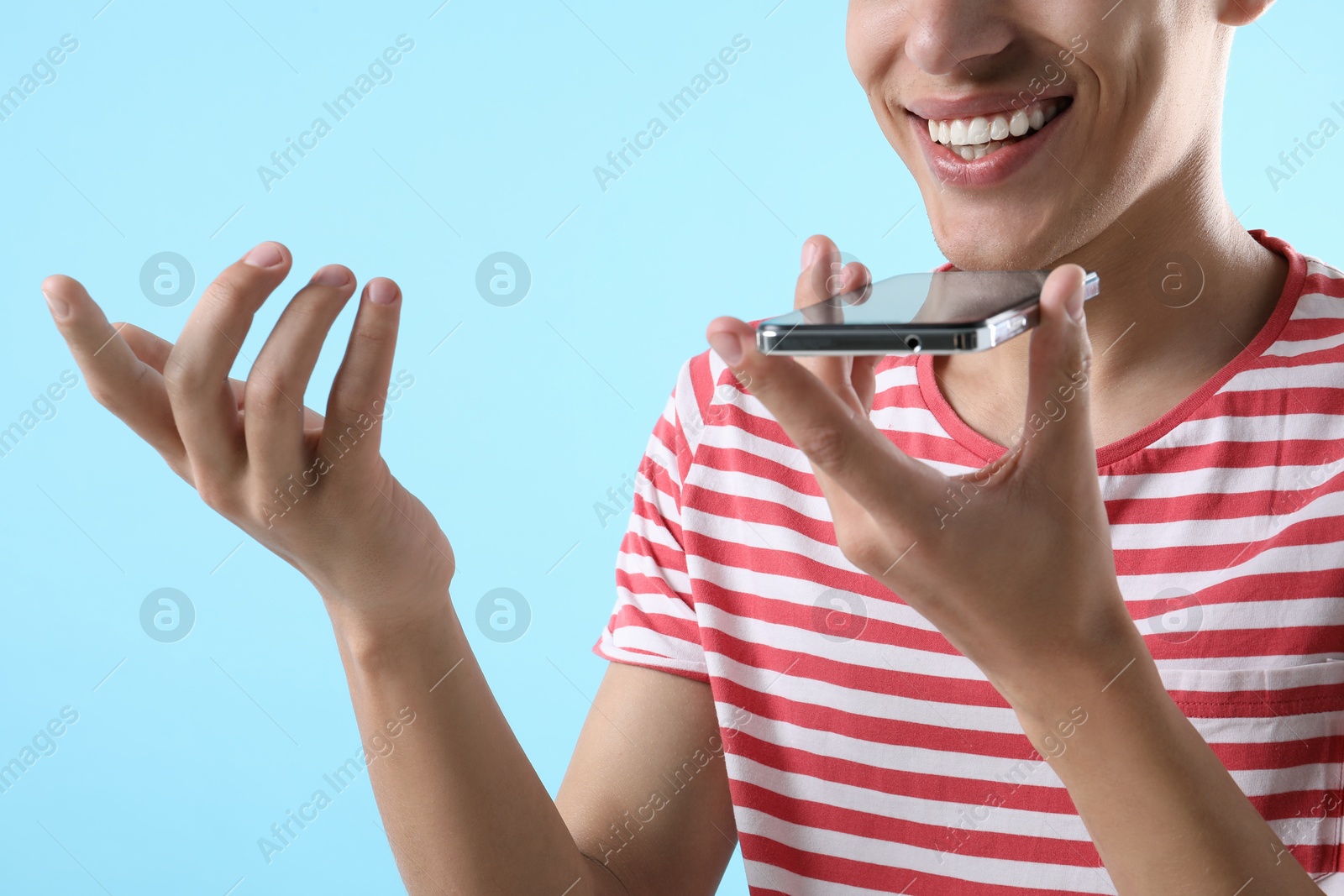 Photo of Young man recording voice message via smartphone on light blue background, closeup