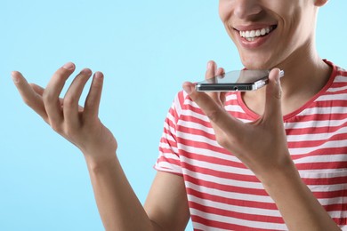 Young man recording voice message via smartphone on light blue background, closeup