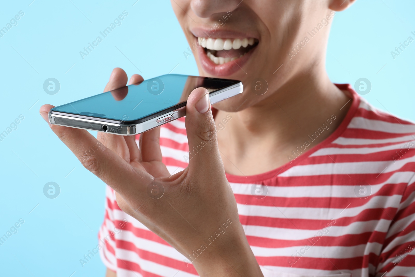 Photo of Young man recording voice message via smartphone on light blue background, closeup