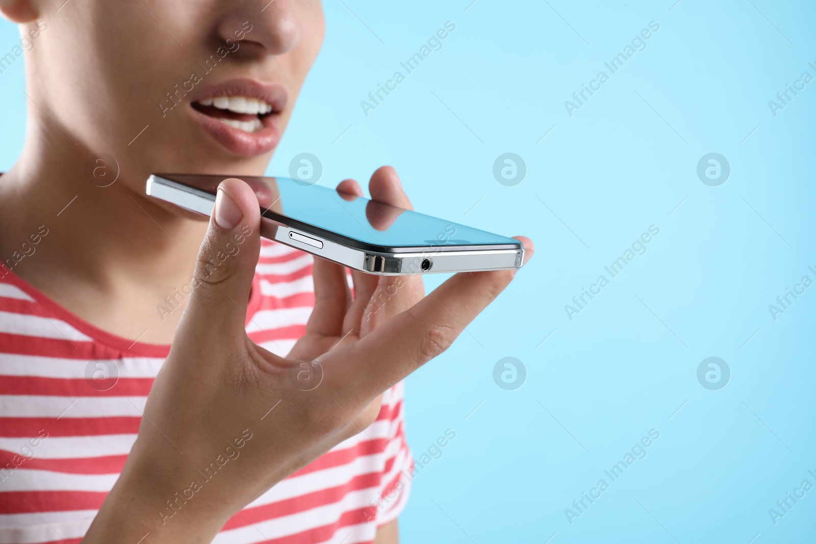 Photo of Young man recording voice message via smartphone on light blue background, closeup. Space for text