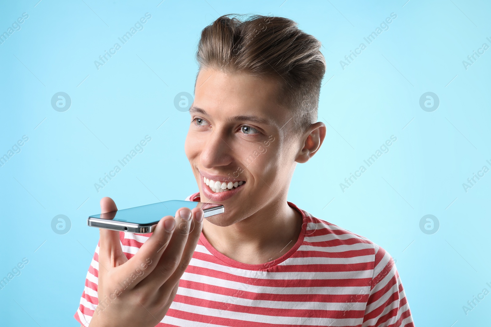 Photo of Young man recording voice message via smartphone on light blue background