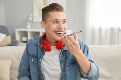 Photo of Young man recording voice message via smartphone at home