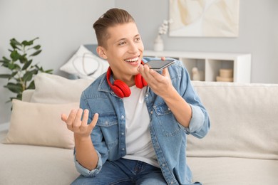 Young man recording voice message via smartphone at home