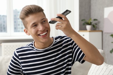 Young man with smartphone listening to voice message at home