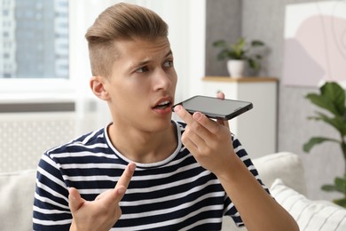 Young man recording voice message via smartphone at home