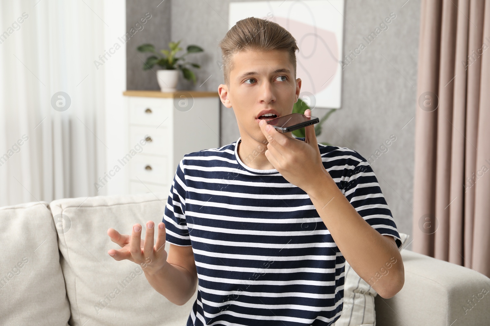 Photo of Young man recording voice message via smartphone at home