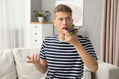 Young man recording voice message via smartphone at home