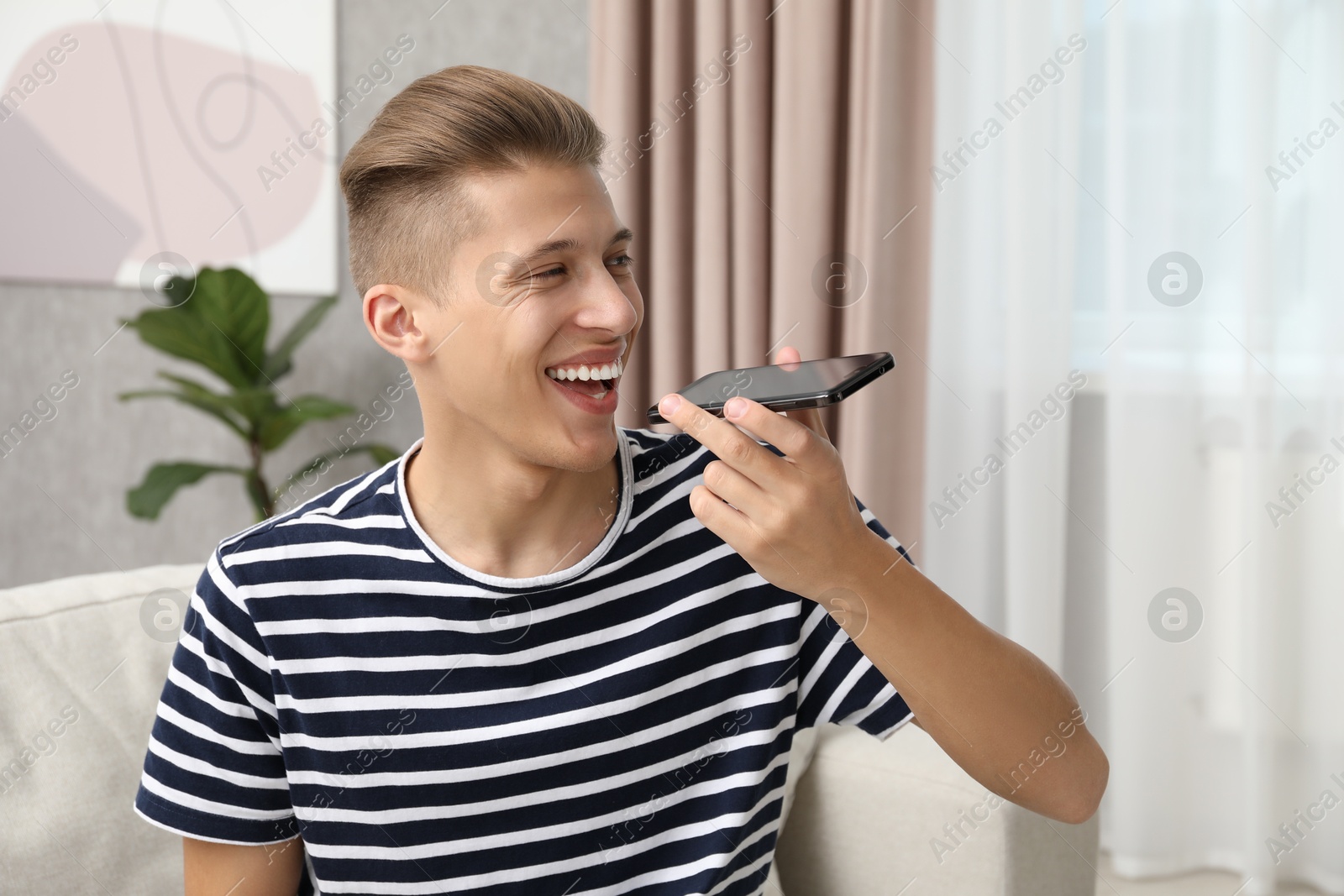 Photo of Young man recording voice message via smartphone at home