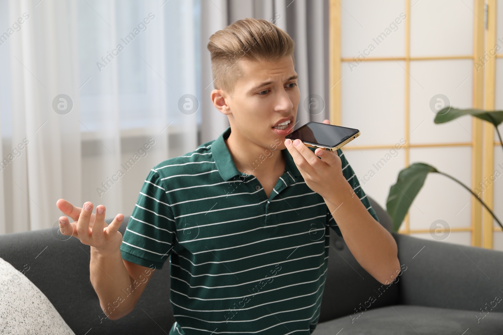 Photo of Young man recording voice message via smartphone at home