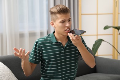 Young man recording voice message via smartphone at home