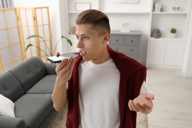 Photo of Young man recording voice message via smartphone at home