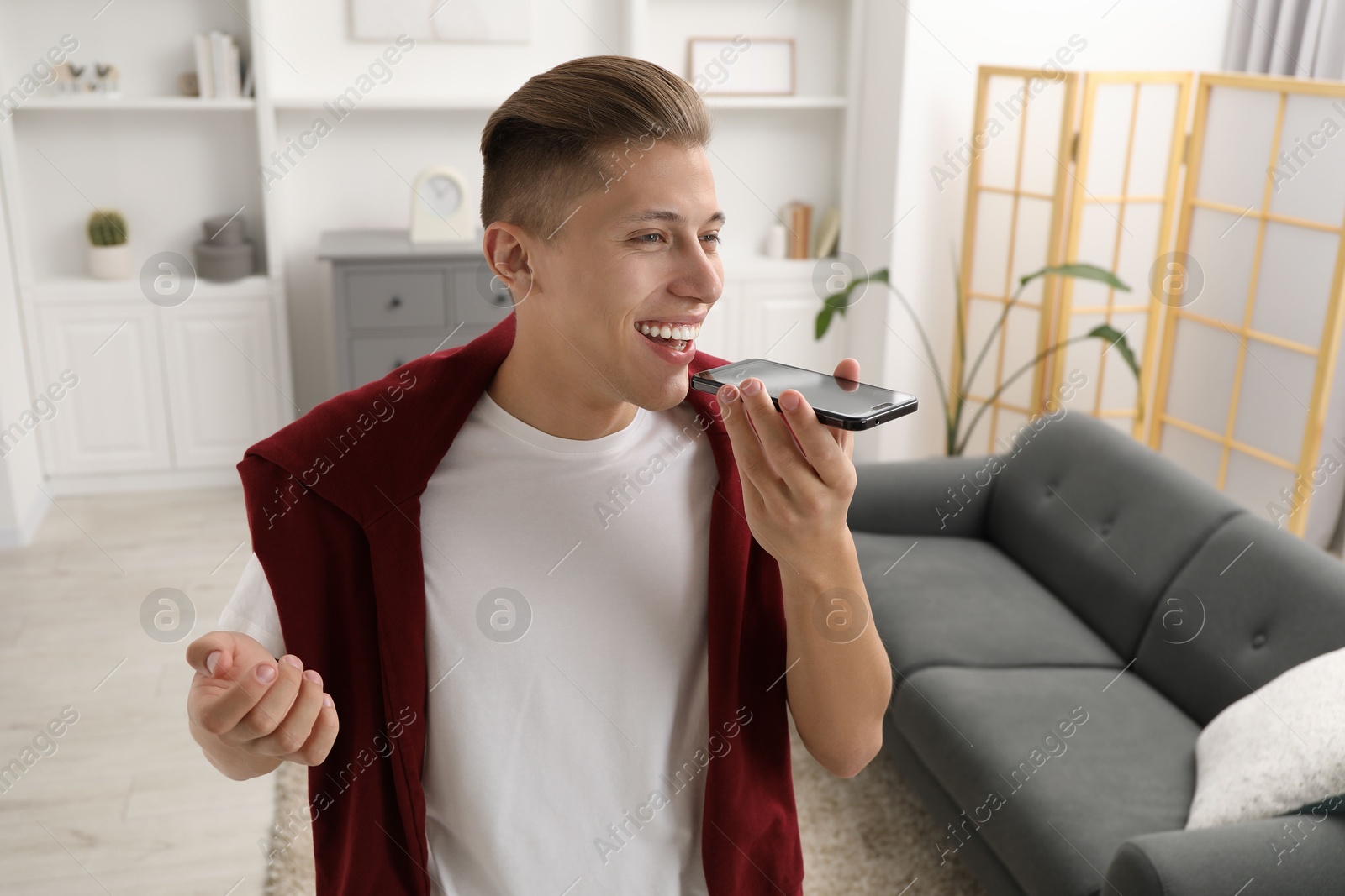 Photo of Young man recording voice message via smartphone at home