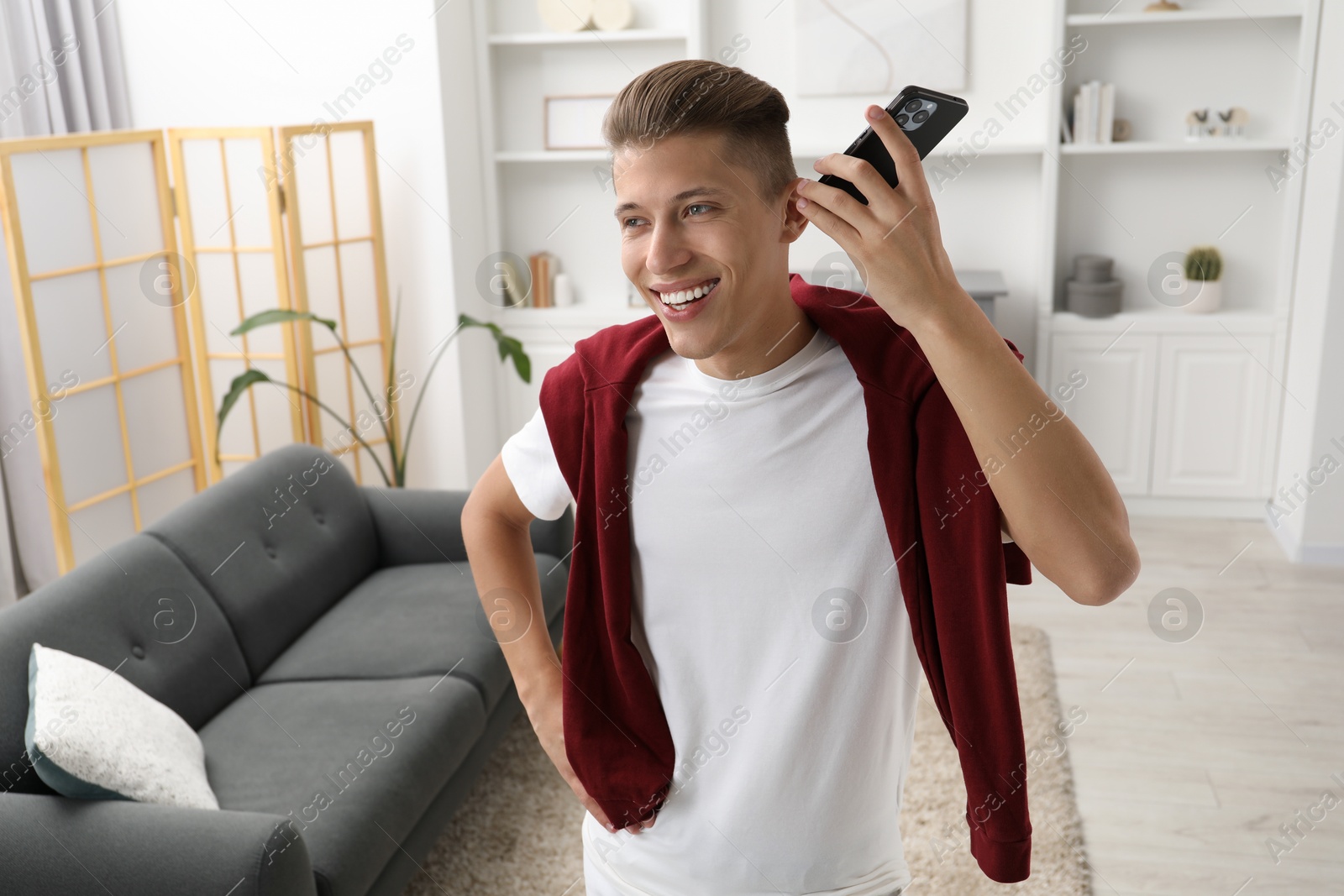 Photo of Young man with smartphone listening to voice message at home