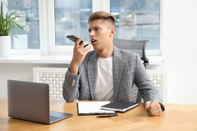 Young man recording voice message via smartphone in office