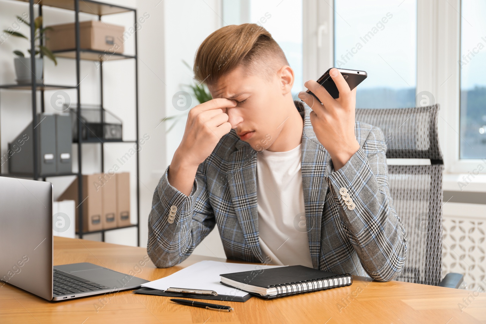 Photo of Young man with smartphone listening to voice message in office