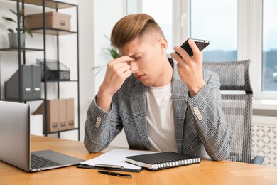 Photo of Young man with smartphone listening to voice message in office