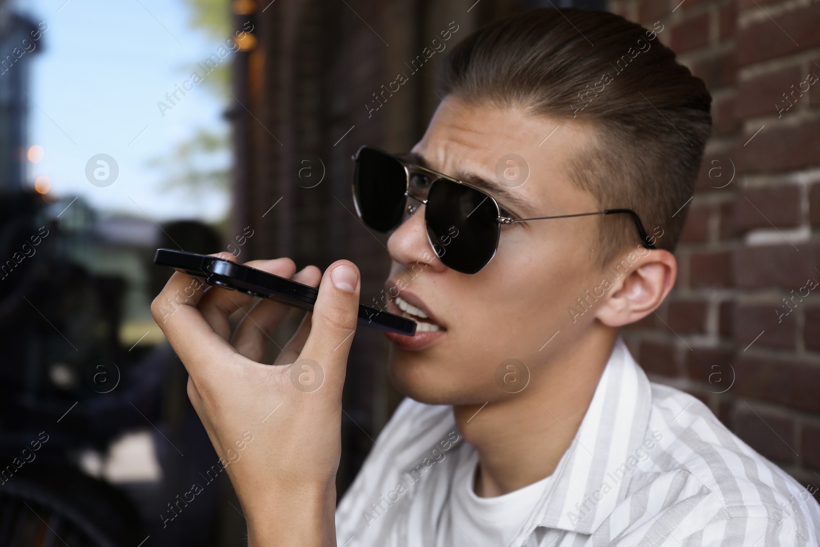 Photo of Young man recording voice message via smartphone in outdoor cafe