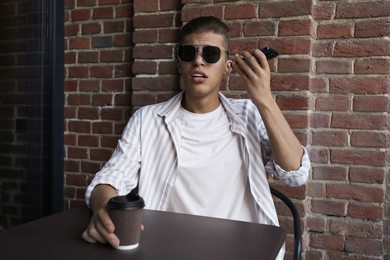 Young man with smartphone listening to voice message in outdoor cafe