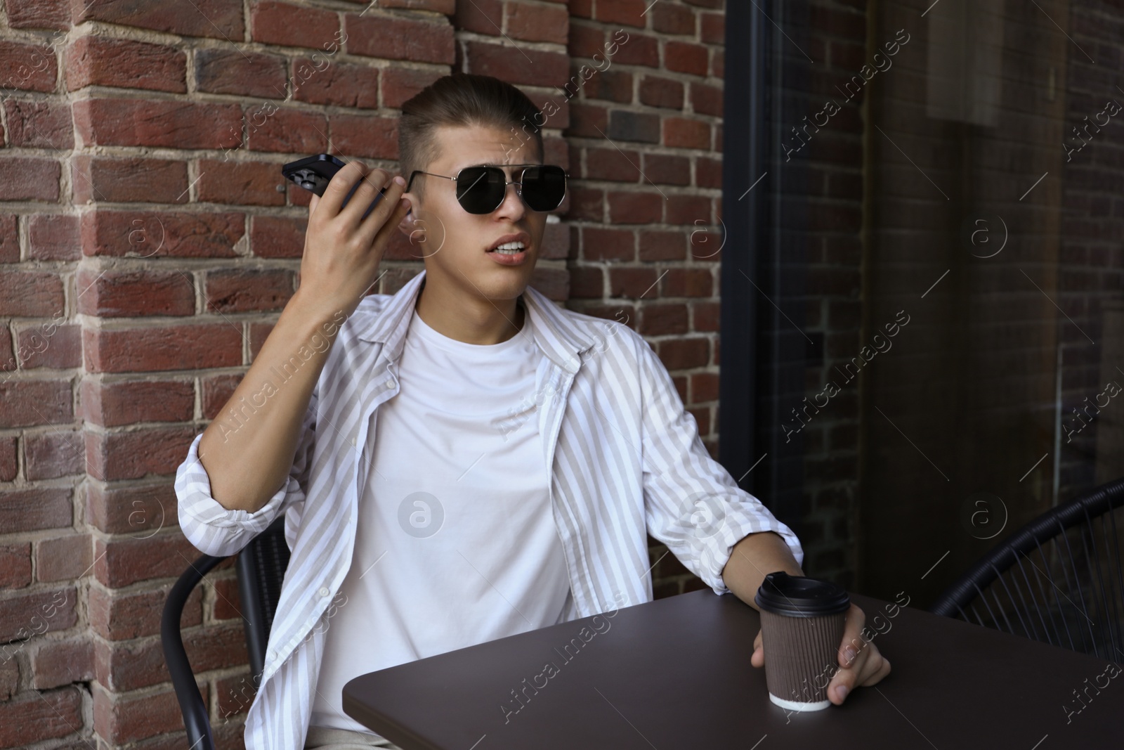 Photo of Young man with smartphone listening to voice message in outdoor cafe