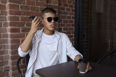 Photo of Young man with smartphone listening to voice message in outdoor cafe