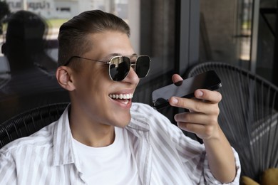 Photo of Young man recording voice message via smartphone in outdoor cafe