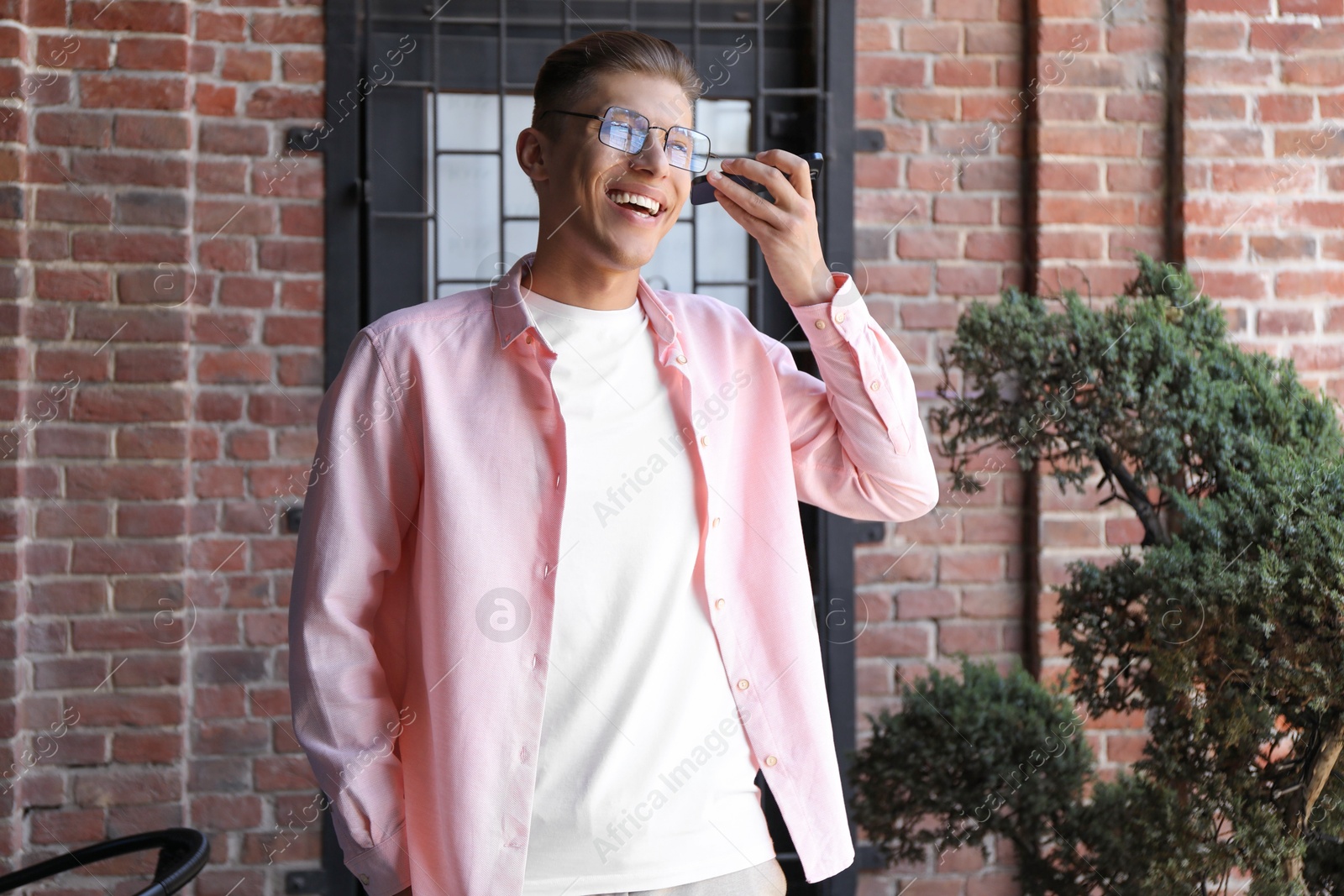 Photo of Young man with smartphone listening to voice message outdoors