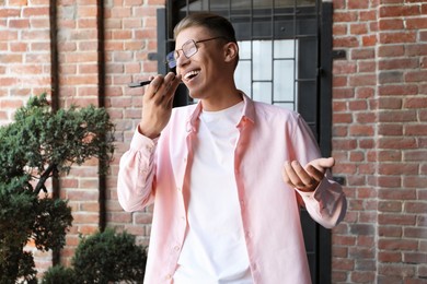 Young man recording voice message via smartphone outdoors